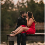 Engagement portrait of couple kissing while seated on a dock at sunset by Coastal Chic Studios