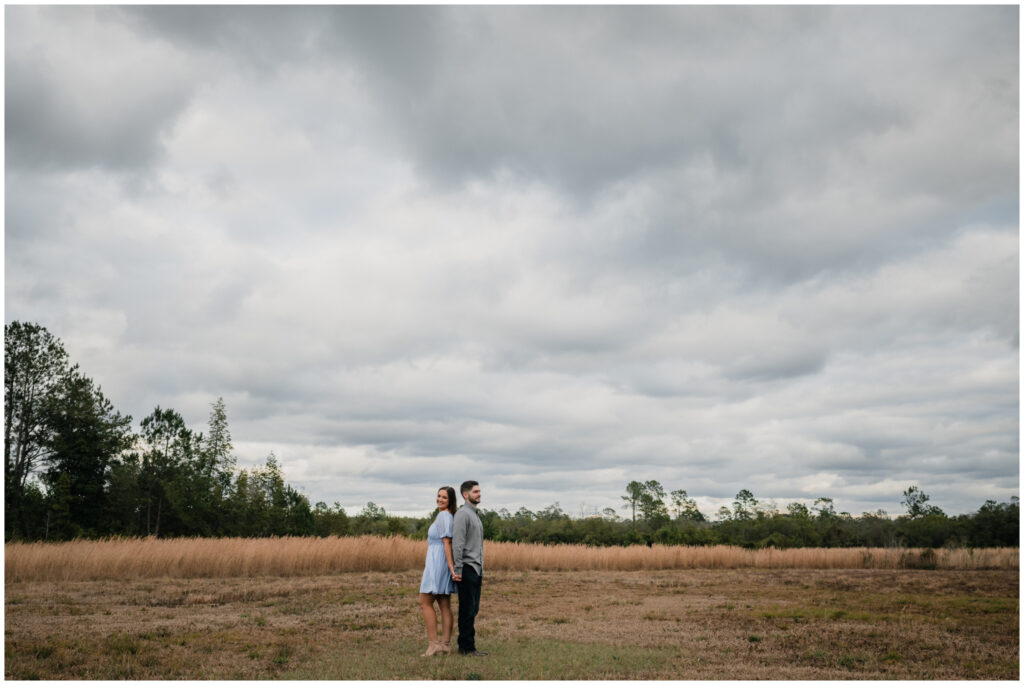 Wide image of an Engagement portrait in a field by Coastal Chic Studios