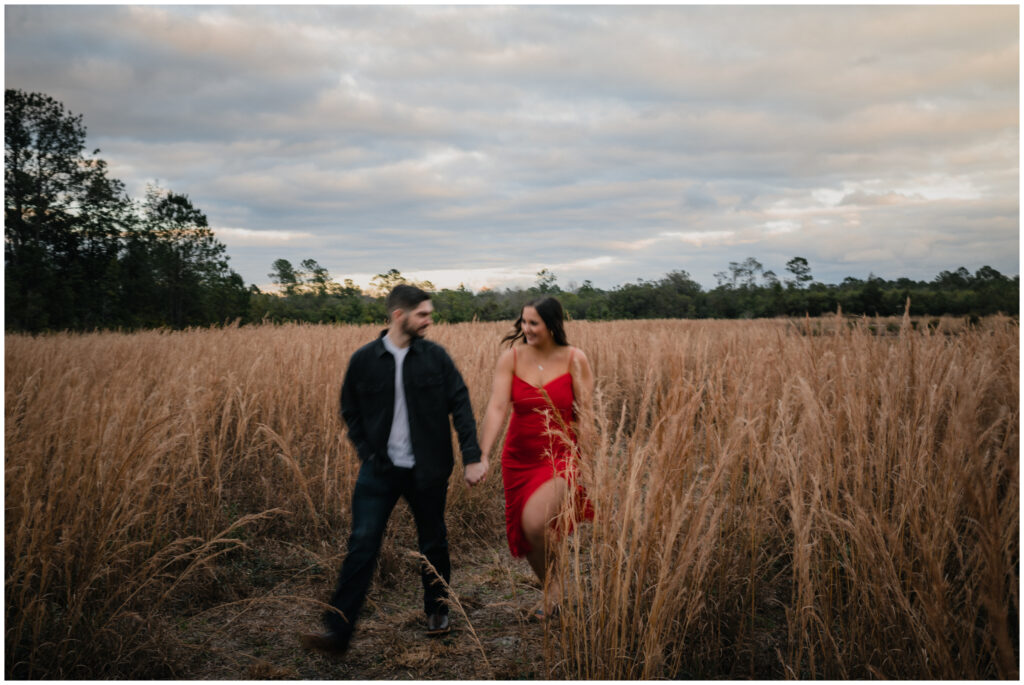 blurred Wide image of an Engagement couple running in a field by Coastal Chic Studios